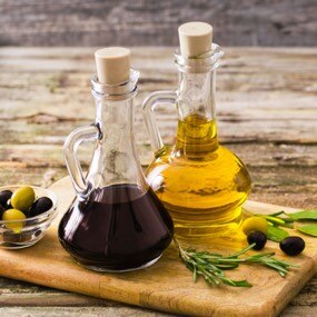 Lahve s olivovým olejem a octem na dřevěné desce.