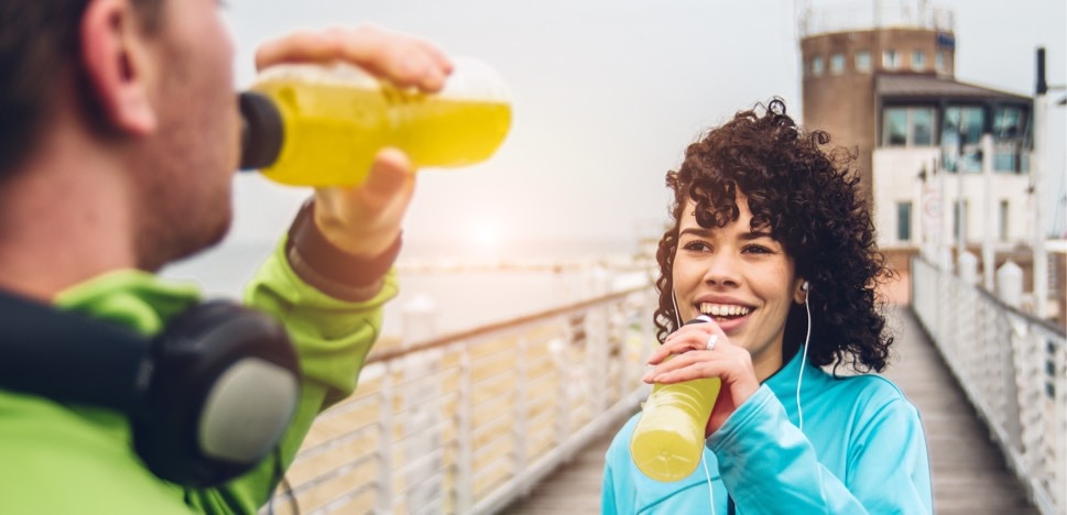 Muž a žena pijící na molu energetické nápoje po sportovní aktivitě.