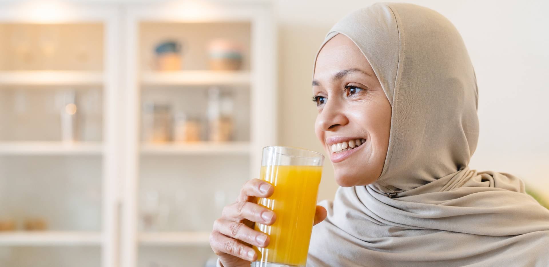 Úsměvavá žena v hidžábu držící sklenici s pomerančovým džusem.