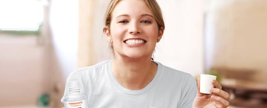 Žena se usmívá a drží ústní vodu a kelímek.