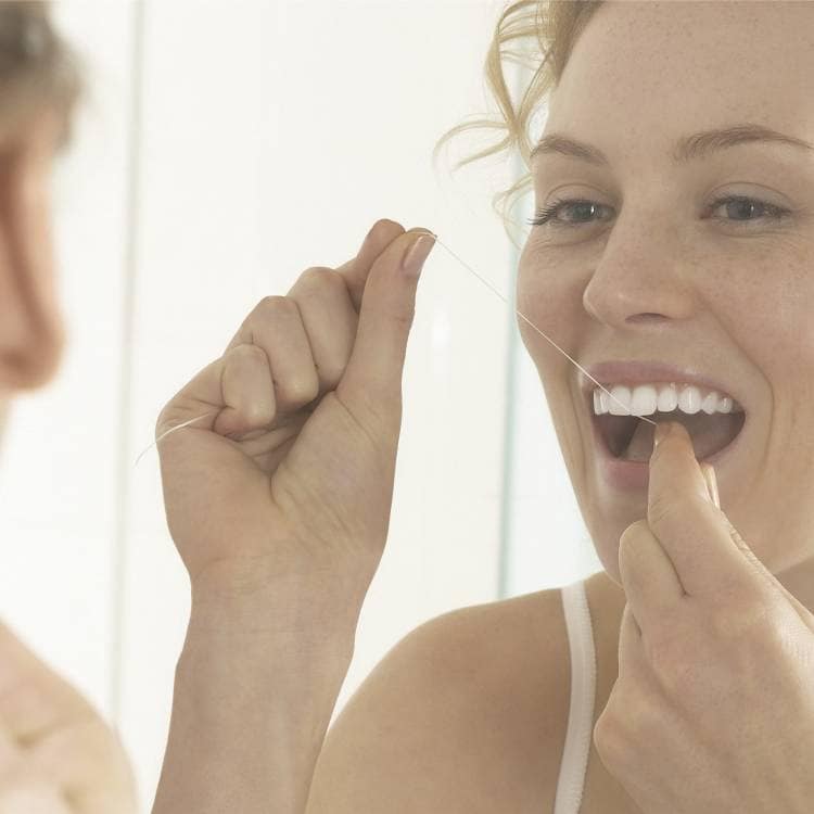 Žena používá dentální nit k čištění mezizubních prostorů.