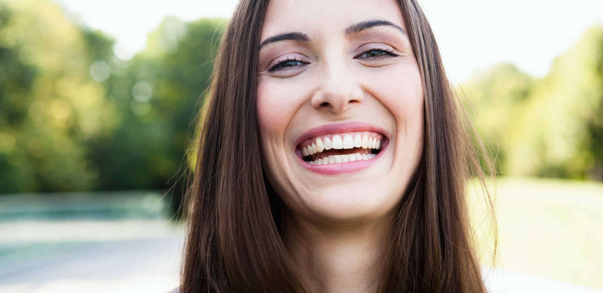 Šťastná žena s dokonalým úsměvem ukazující zdravé zuby na pozadí přírody