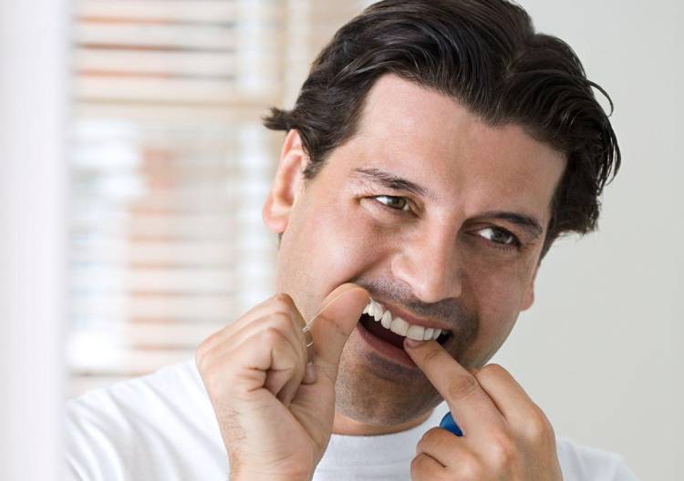 Muž používající dentální nit k čištění mezer mezi zuby.