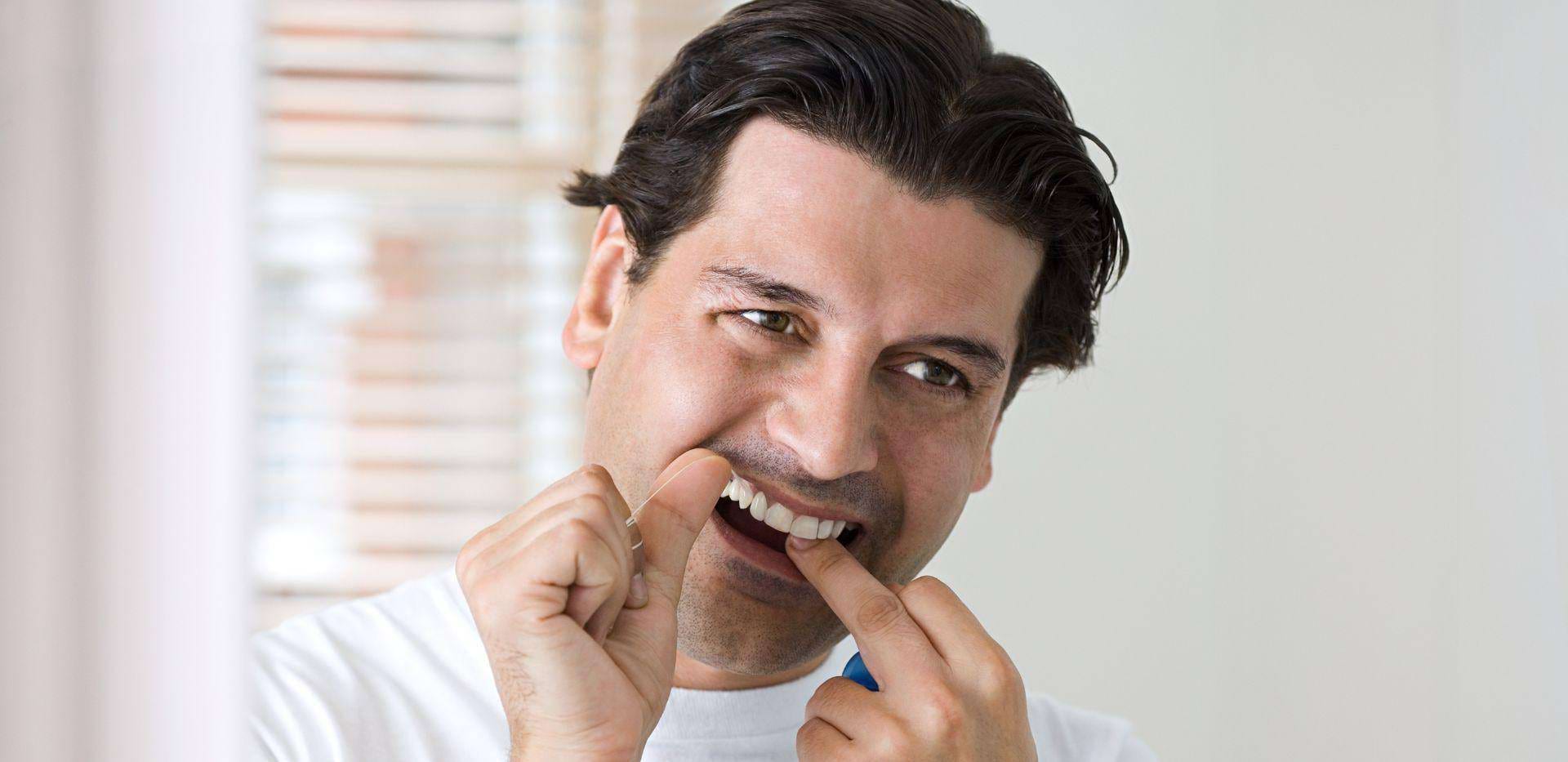 Muž používající dentální nit k čištění mezer mezi zuby.