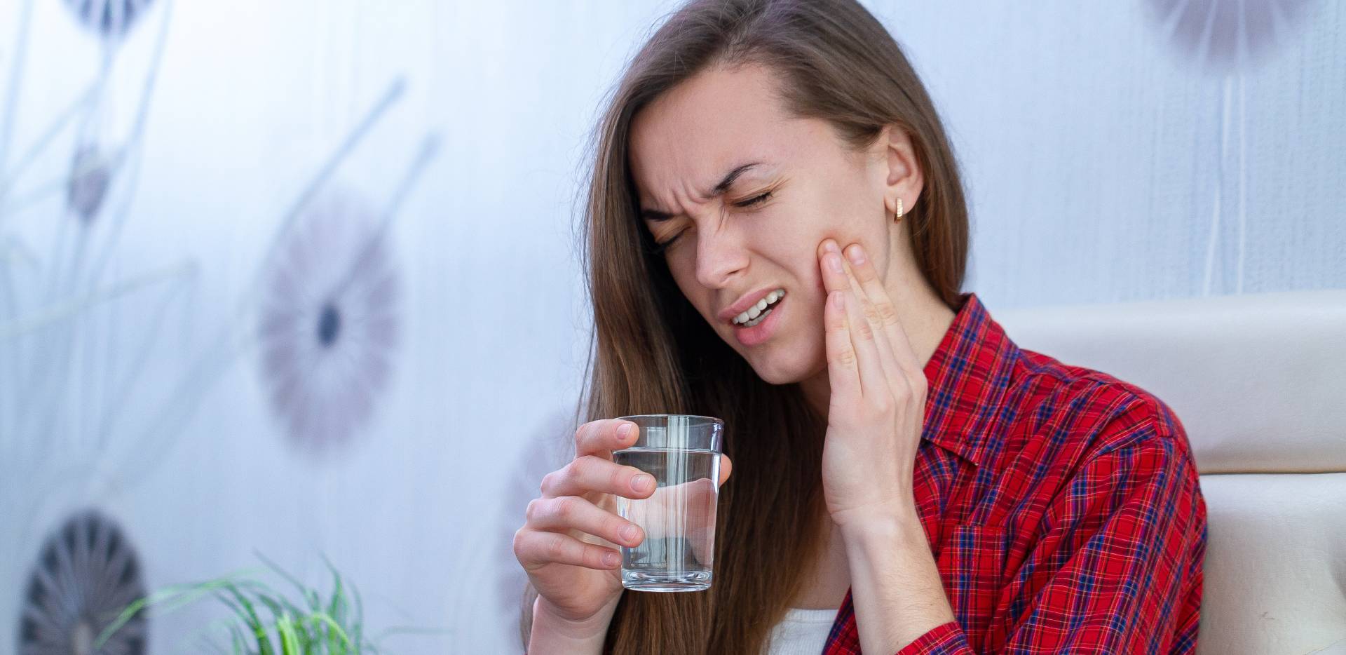 Žena trpí bolestí zubů a drží sklenici vody.